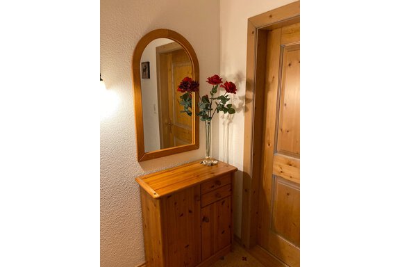 A cozy entrance area with a wooden cabinet and a framed mirror. On the cabinet stands a vase with red roses. - App. Diamant Obergurgl - Obergurgl 