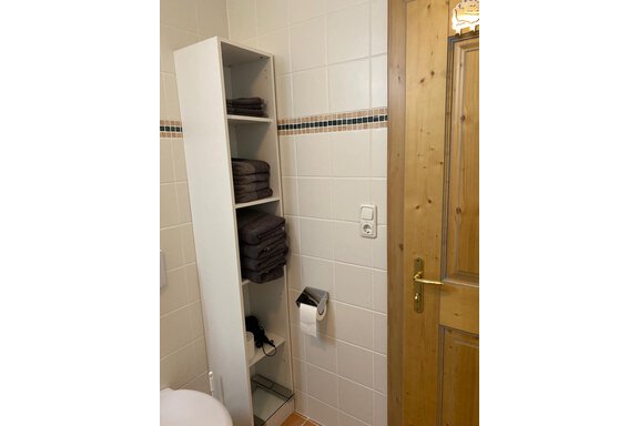 A modern bathroom with a white shelf for towels and a wooden door. On the other side, sanitary facilities are visible. - App. Diamant Obergurgl - Obergurgl 