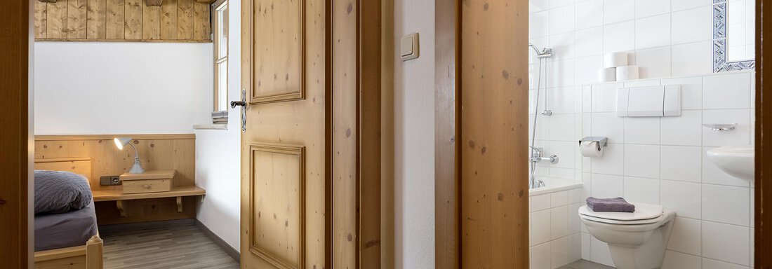 A bright hallway with a wooden floor and visible wooden beams. On the right side is a modern bathroom with a bathtub and a toilet. - Appartementhaus Schalfblick - Obergurgl 