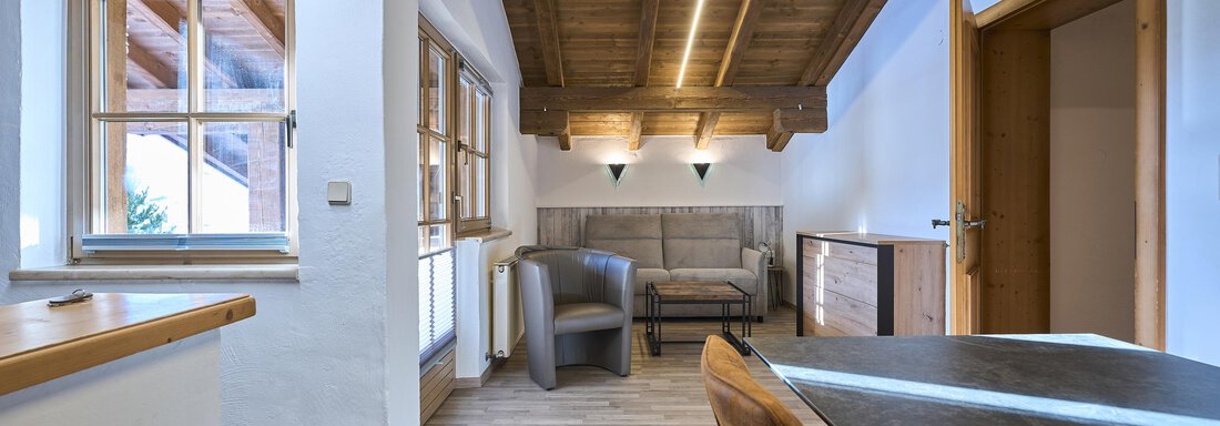A modern living room with wooden ceilings and light walls. There is a cozy couch and a table in the room. - Appartementhaus Schalfblick - Obergurgl 