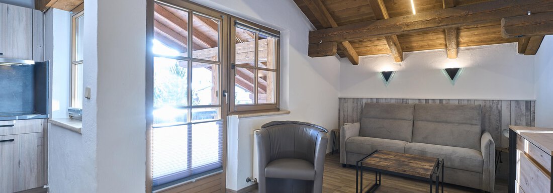A cozy room with wooden ceilings and large windows. There is a sofa and an armchair as well as a small table. - Appartementhaus Schalfblick - Obergurgl 