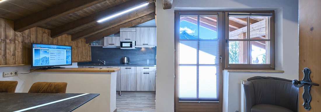 A modern and cozy living and dining room with wooden paneling. The kitchen is open and bright, with large windows that let in plenty of light. - Appartementhaus Schalfblick - Obergurgl 