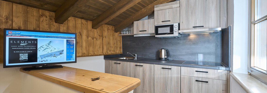 Modern kitchen with wooden ceiling and light cabinets. A television is on the bar counter and there is a microwave. - Appartementhaus Schalfblick - Obergurgl 