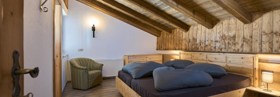 A cozy bedroom with wooden beams and a large bed. There is a chair in the corner and pleasant lighting. - Appartementhaus Schalfblick - Obergurgl 