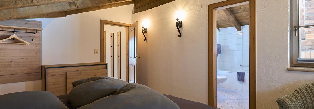 A cozy bedroom with a wooden ceiling and modern design. There is a large bed, a comfortable corner, and access to the bathroom. - Appartementhaus Schalfblick - Obergurgl 