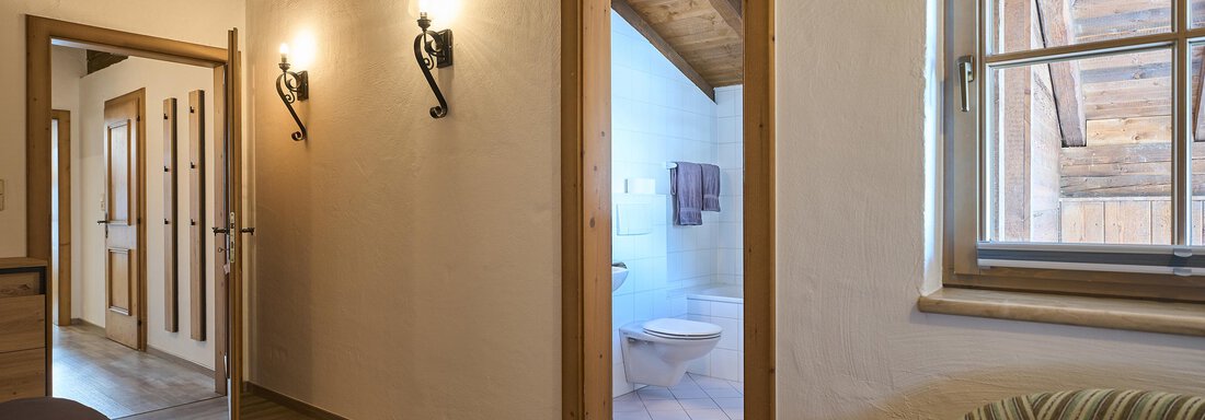 A bright hallway with a wooden beam ceiling and two doors. In the background, a bathroom is visible. - Appartementhaus Schalfblick - Obergurgl 
