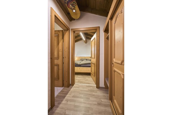 A bright hallway with wooden cabinets and doors. At the end of the hallway, a bedroom is visible. - Appartementhaus Schalfblick - Obergurgl 