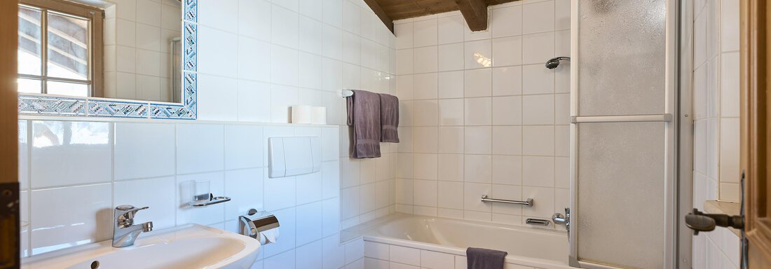 A bright bathroom with a bathtub and shower. The wooden ceiling gives the room a pleasant atmosphere. - Appartementhaus Schalfblick - Obergurgl 