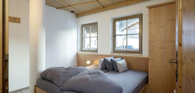 A cozy bedroom with a large double bed and wooden paneling. There are two windows that provide daylight. - Appartementhaus Schalfblick - Obergurgl 