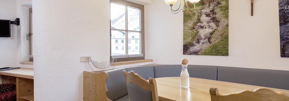 A cozy dining area with a wooden bench and a table. Pictures of nature hang on the walls, and there is plenty of daylight. - Appartementhaus Schalfblick - Obergurgl 