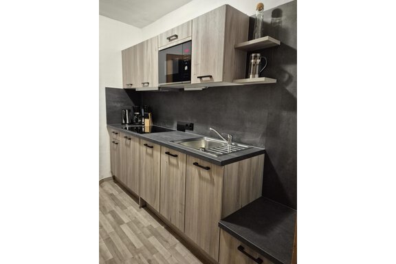 A modern kitchen with wooden fronts and a stainless steel sink. Electric appliances such as a microwave and coffee machine are also available. - Appartementhaus Schalfblick - Obergurgl 