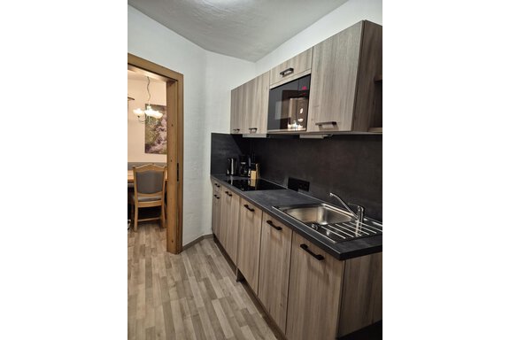 A modern kitchen with wooden cabinets and a sleek workspace. In the background, a dining area is visible. - Appartementhaus Schalfblick - Obergurgl 