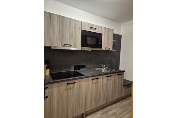 A modern kitchen with wooden fronts and a stainless steel sink. It includes a stove, a microwave, and ample storage space. - Appartementhaus Schalfblick - Obergurgl 
