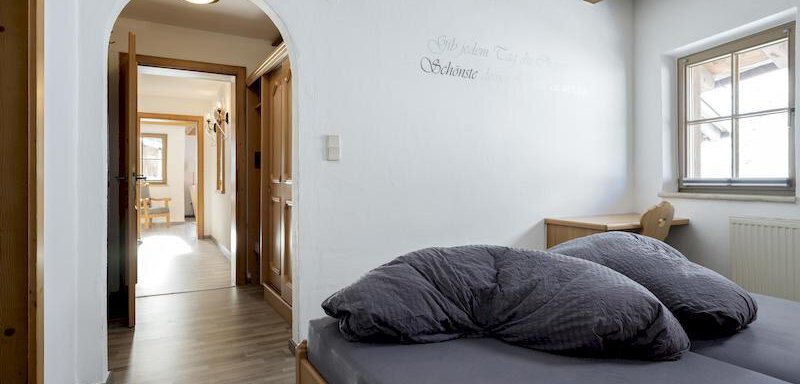 A cozy bedroom with a double bed and large pillows. In the background, you can see the access to a bright hallway and other rooms. - Appartementhaus Schalfblick - Obergurgl 