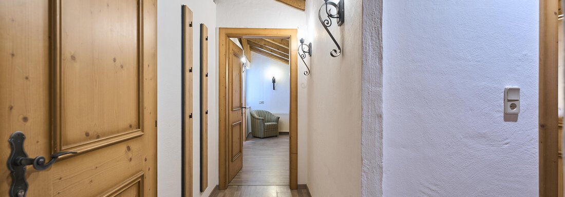 A bright hallway with wooden doors and a wooden ceiling. At the end of the hallway, another room is visible. - Appartementhaus Schalfblick - Obergurgl 
