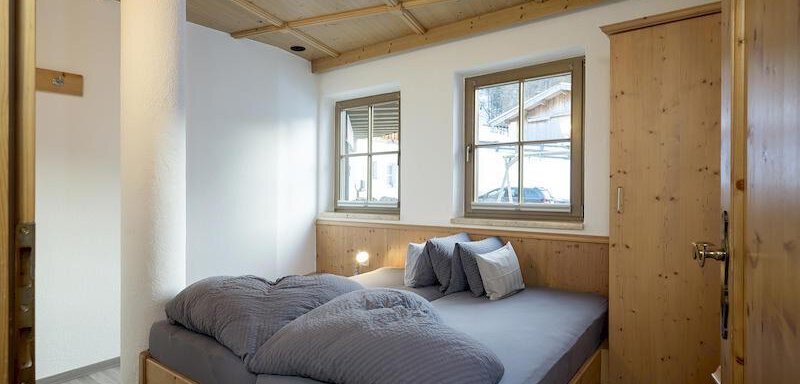 A cozy bedroom with a large double bed and wooden details. There are two windows that let in daylight. - Appartementhaus Schalfblick - Obergurgl 