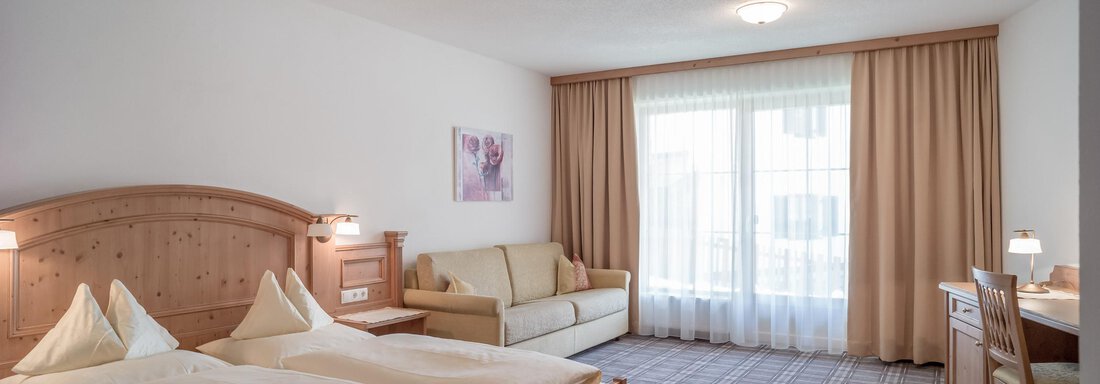 A modern hotel room with a double bed, a sofa, and a desk. Large windows provide plenty of daylight. - Ferienwohnung de Luxe Alpenresidenz am Mühlbach - Obergurgl 