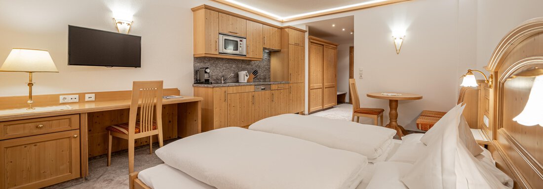 A modern room with two single beds and wooden furniture. There is a table, a chair, and a small kitchenette. - Ferienwohnung de Luxe Alpenresidenz am Mühlbach - Obergurgl 
