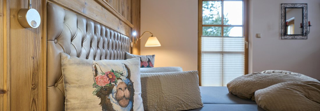 Appartement Alpenwald | © Andreas Sillaber, Privat (CC C) A cozy bedroom with a wooden wall panel and a padded headboard. A decorative pillow is placed on the bed, and the window lets in a lot of daylight. - Forest Chalet - Obergurgl