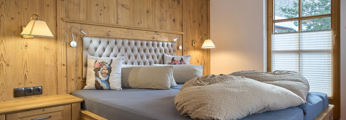 A cozy bedroom with a large bed and wooden paneling. Two nightstands with lamps and a window that lets in plenty of light. - Forest Chalet - Obergurgl 