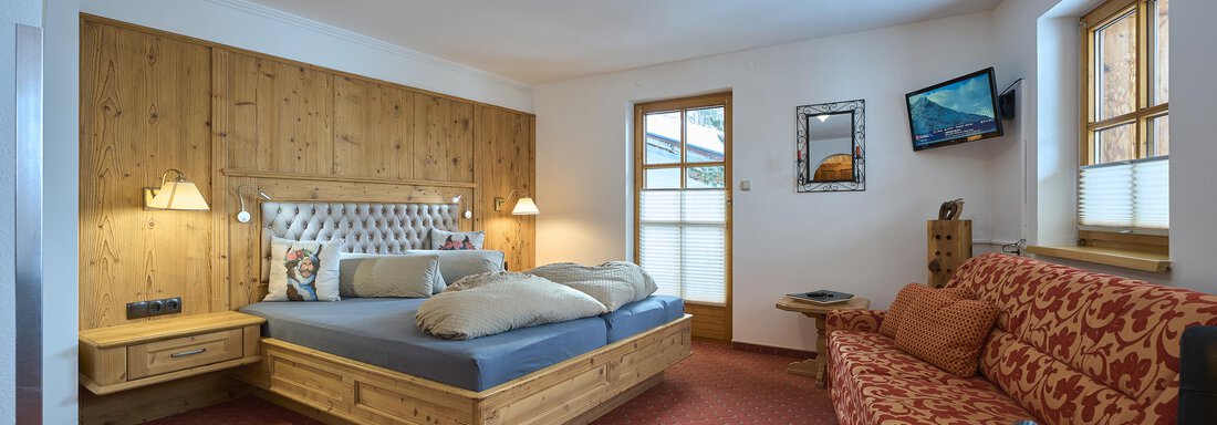 A cozy bedroom with a double bed and a red sofa. The room has large windows that let in plenty of daylight. - Forest Chalet - Obergurgl 