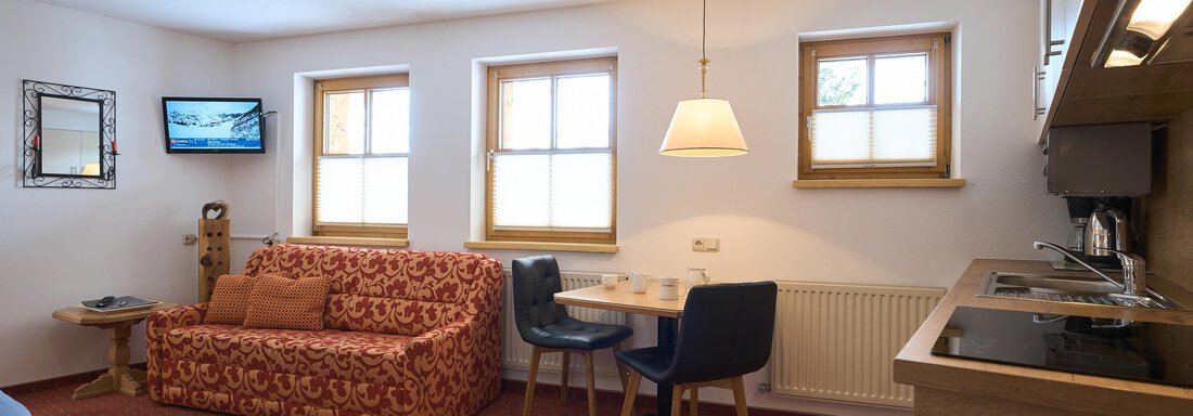 A bright living room with a red sofa and a table. There is a television on the wall and the kitchen is open plan. - Forest Chalet - Obergurgl 