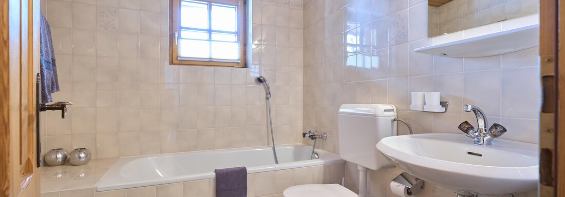 A bathroom with a bathtub, a sink, and a shower. The walls are light-tiled and there are wooden details on the ceiling. - Forest Chalet - Obergurgl 