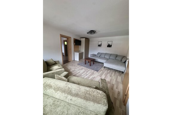 A modern living room with a large couch and a small table. The room is bright and friendly, with wooden flooring and minimalist decor. - Forest Chalet - Obergurgl 