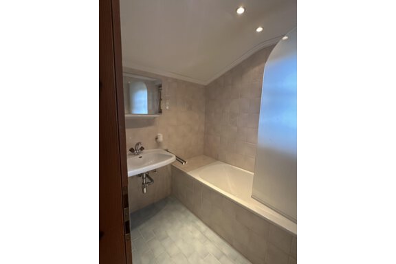 A modern bathroom with a bathtub and a sink. The walls are tiled in light, neutral colors. - Forest Chalet - Obergurgl 