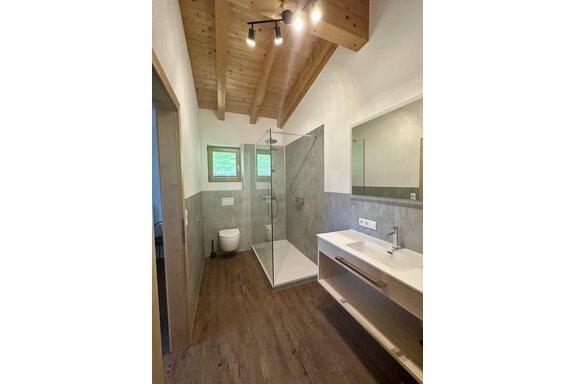 A modern bathroom with a glass shower and wooden ceiling.  
It features a bright color scheme and plenty of natural light. - Forest Chalet - Obergurgl 