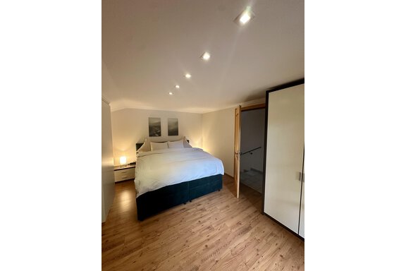 A modern bedroom with a large bed and warm wooden flooring. The walls are light, and there is a wardrobe door as well as soft lighting. - Forest Chalet - Obergurgl 