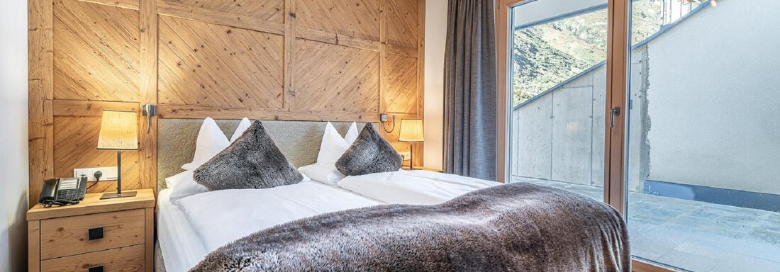 Apt_1_SZ A cozy bedroom with a double bed and modern wooden details. Large windows provide plenty of daylight and access to the terrace. - Gletscherblick - Serviced Apartments - Obergurgl