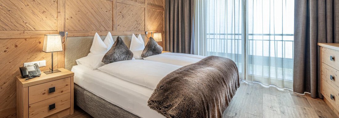 A cosy room with two beds and wooden paneling. Large windows allow for plenty of daylight and provide a balcony view. - Gletscherblick - Serviced Apartments - Obergurgl 