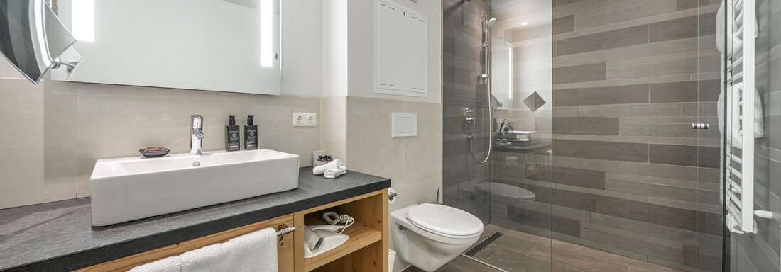 A modern bathroom with a large shower and an elegant sink. The walls are in neutral colors and reflect a contemporary style. - Gletscherblick - Serviced Apartments - Obergurgl 