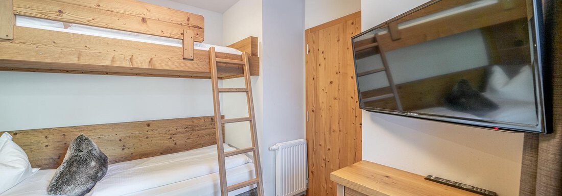 A cozy bedroom with a wooden loft bed and a flat-screen TV. The room is bright and modernly furnished. - Gletscherblick - Serviced Apartments - Obergurgl 