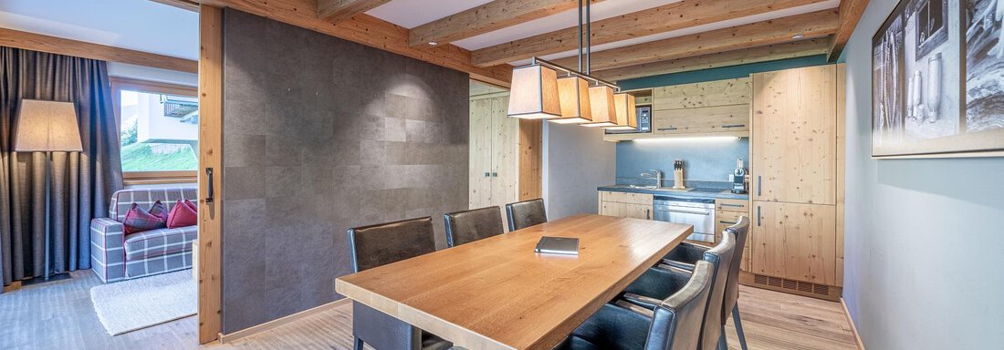 A modern dining area with a long wooden table and black chairs. Ceiling beams and a cozy atmosphere give the room an inviting character. - Gletscherblick - Serviced Apartments - Obergurgl 