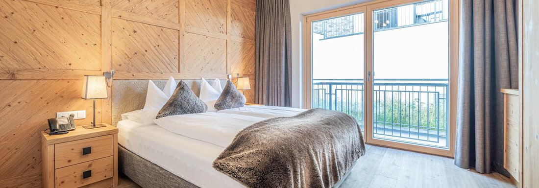 Apt_4_SZ A cozy bedroom with a large double bed and warm wooden walls. Large windows offer plenty of daylight and a view of the balcony. - Gletscherblick - Serviced Apartments - Obergurgl