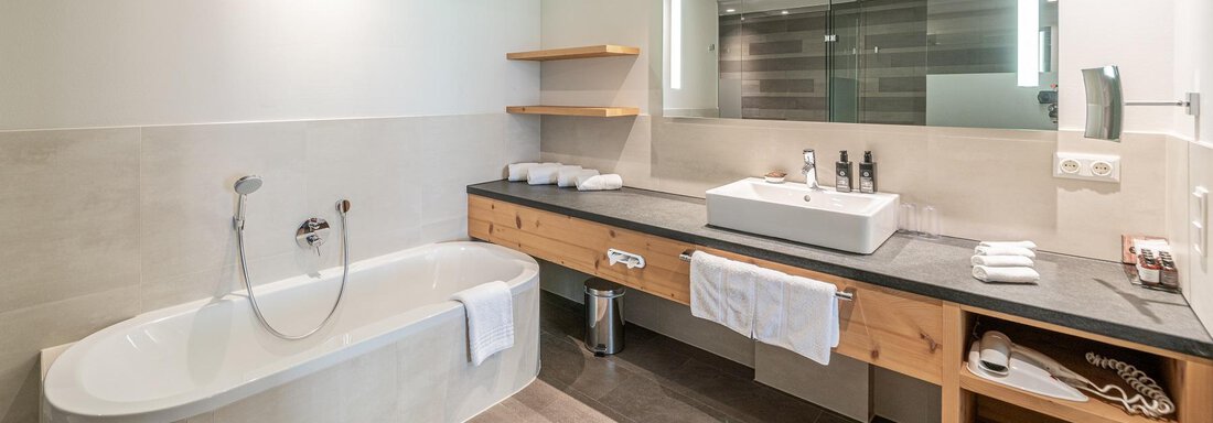 A modern bathroom with a freestanding bathtub and an elegant sink. The soft lighting and clean lines create a relaxing atmosphere. - Gletscherblick - Serviced Apartments - Obergurgl 