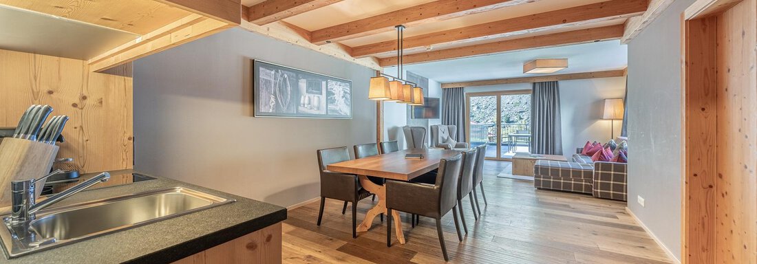Apt_5_Wohnen A modern kitchen with wooden surfaces and a large dining table. The space is bright and inviting, with a cozy living room in the background. - Gletscherblick - Serviced Apartments - Obergurgl