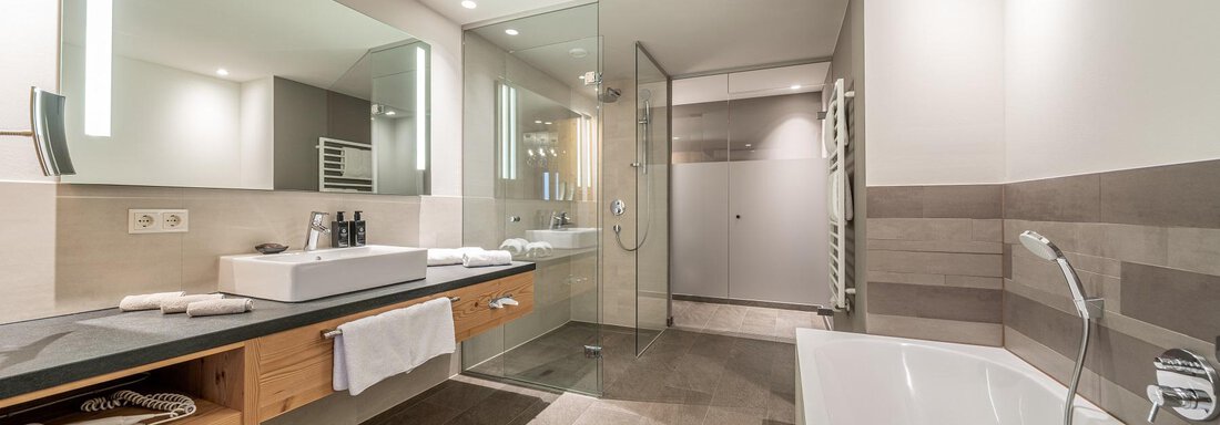 A modern bathroom with a shower, a bathtub, and a double sink. The decor is elegant and contemporary. - Gletscherblick - Serviced Apartments - Obergurgl 