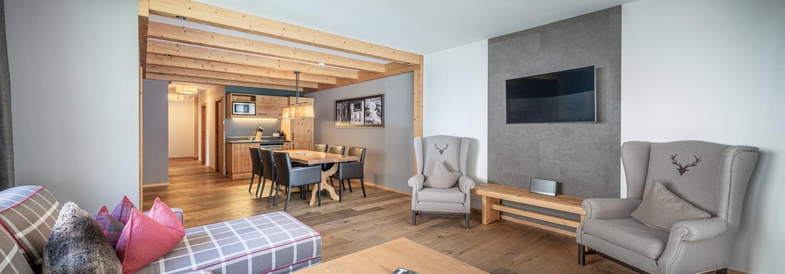 A modern living space with a comfortable sofa and two elegant armchairs. In the background, there is a dining table and an open kitchen. - Gletscherblick - Serviced Apartments - Obergurgl 