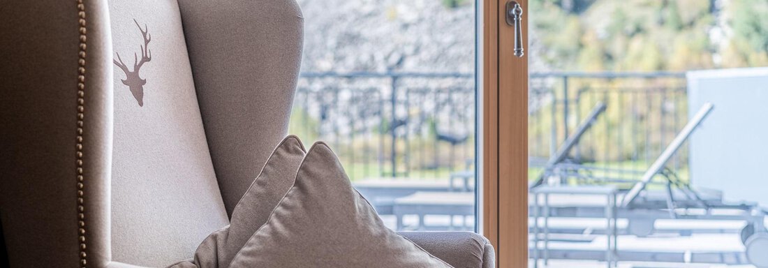 Apt_6_Detail A cozy armchair with a decorative cushion is set in front of large windows. Through the windows, a beautiful view of the surroundings is visible. - Gletscherblick - Serviced Apartments - Obergurgl