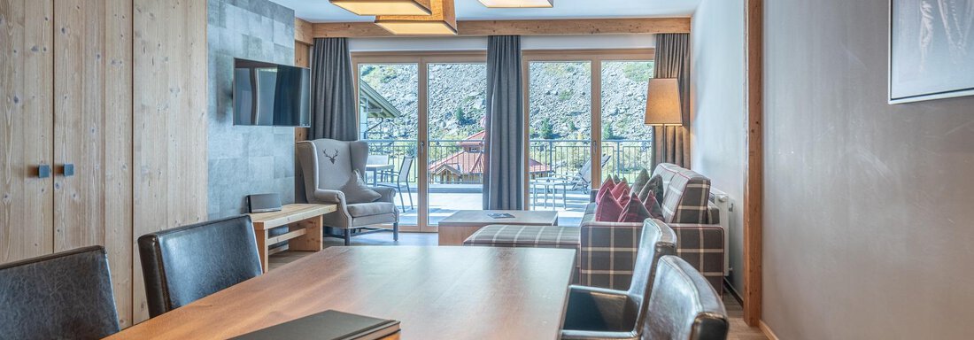 A modern room with a large table and stylish chairs. Large windows offer a view of the terrace and the outdoor area. - Gletscherblick - Serviced Apartments - Obergurgl 