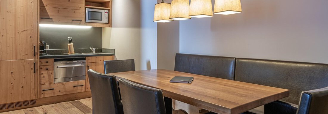 Apt_7_Detail A cozy kitchen with wooden shelves and a dining area. The table is made of wood and surrounded by black chairs. - Gletscherblick - Serviced Apartments - Obergurgl