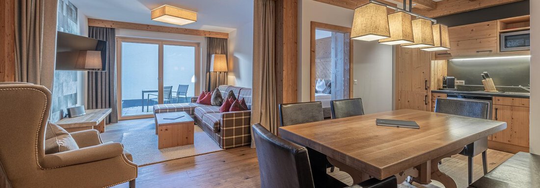 A cozy living and dining room with wooden beams and modern furniture. The room features large windows that let in daylight and offer a terrace with a view. - Gletscherblick - Serviced Apartments - Obergurgl 
