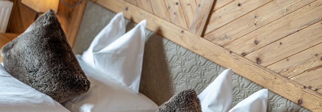 A cozy bedroom with two beds and decorative cushions. The wall is made of wood, creating a warm atmosphere. - Gletscherblick - Serviced Apartments - Obergurgl 