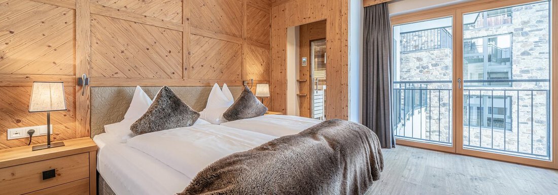 Apt_9_SZ A cozy bedroom with a large bed and wooden walls. Large window with a view outside and a relaxing atmosphere. - Gletscherblick - Serviced Apartments - Obergurgl