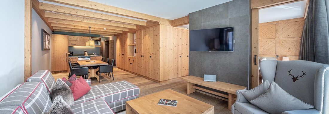 A modern living room with wooden design and cozy furniture. The furnishings include a couch, a television, and a dining table. - Gletscherblick - Serviced Apartments - Obergurgl 