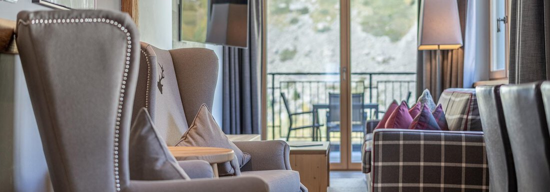 Apt_10_Detail A modern living room with cozy armchairs and a sofa. Large windows offer a view of the balcony and the outdoor scenery. - Gletscherblick - Serviced Apartments - Obergurgl