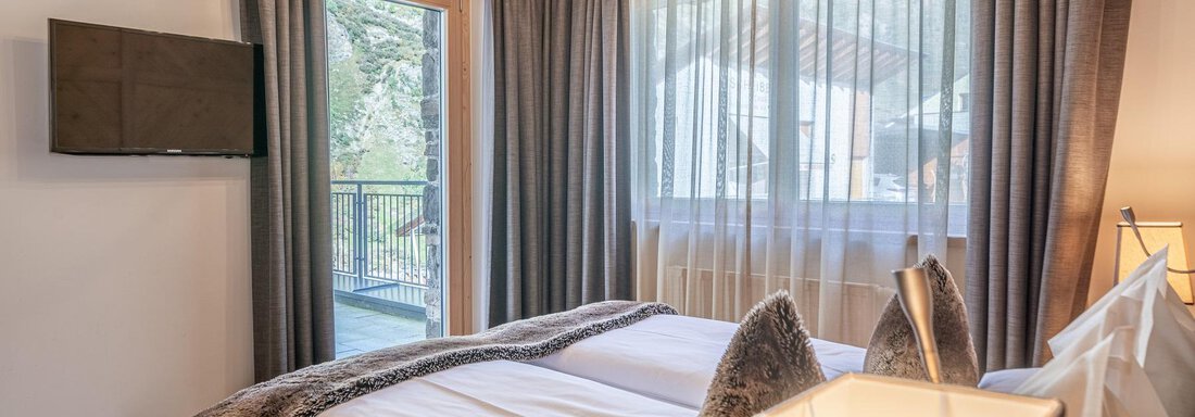 A cozy bedroom with a double bed and a television on the wall.  
Large windows let in plenty of daylight and provide a view outside. - Gletscherblick - Serviced Apartments - Obergurgl 